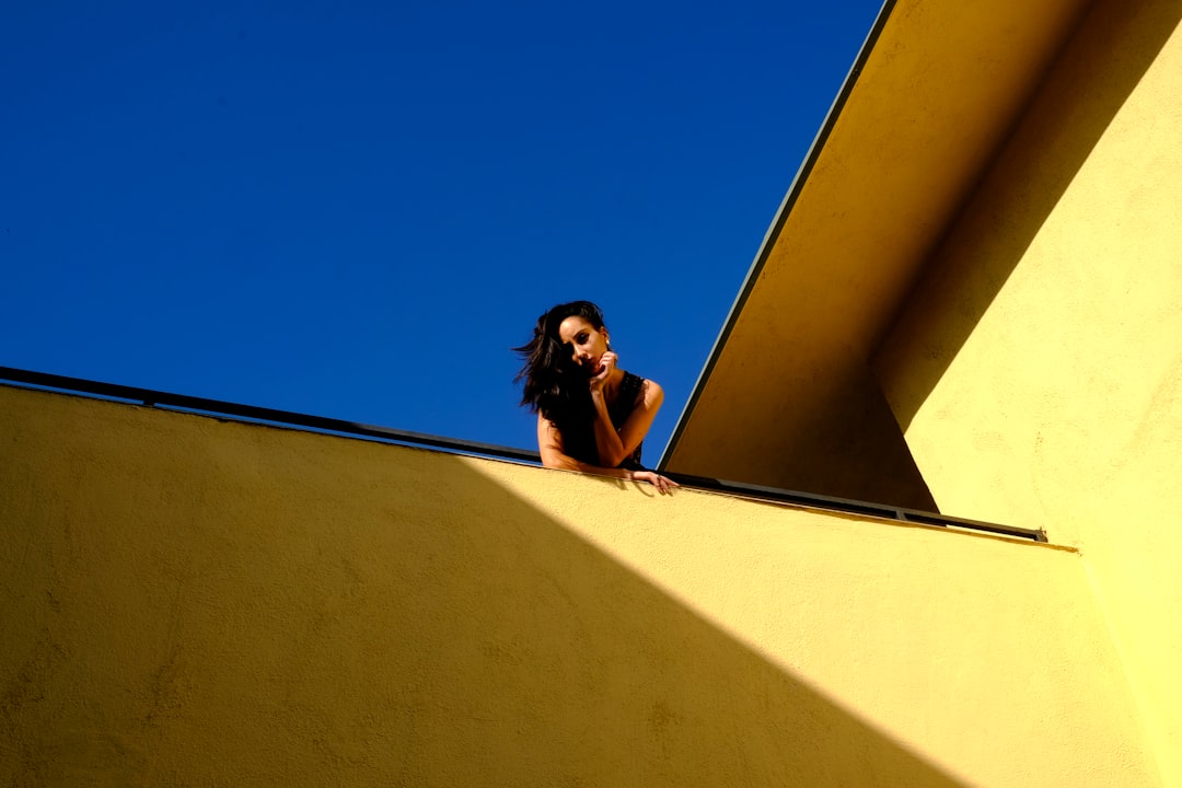 A homeowner looking thoughtfully through the large window of a modern house, conveying the feeling of being 'stuck' or in 'golden handcuffs' despite having a valuable asset.